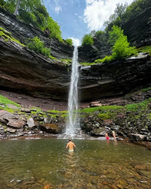 Swimmers in a natural pool below a waterfall